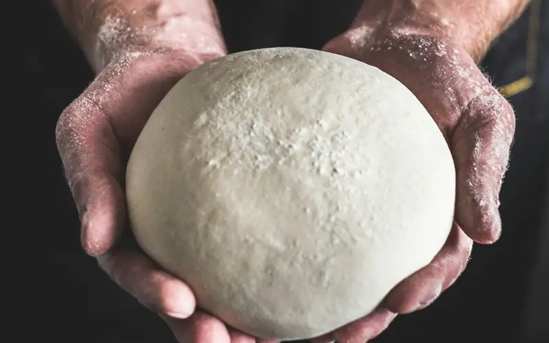 Twee handen houden een bol pizzadeeg vast tegen een donkere achtergrond
