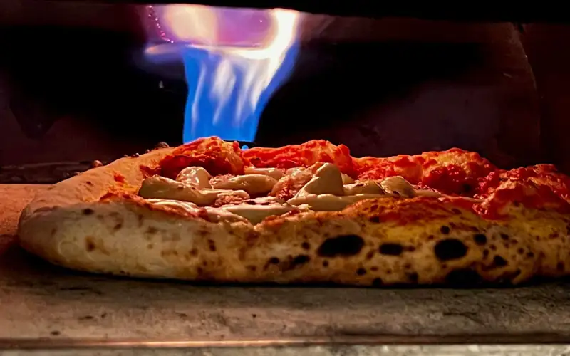 Blauwe gasvlam boven een pizza met luchtige rand in een oven
