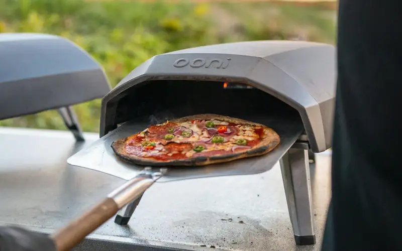 Zelfgemaakte pizza op een schep voor een draagbare gasoven van Ooni, buiten op een tafel
