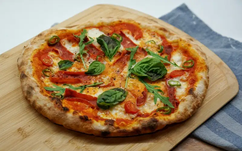 Pizza met tomaat en basilicum op een houten plank